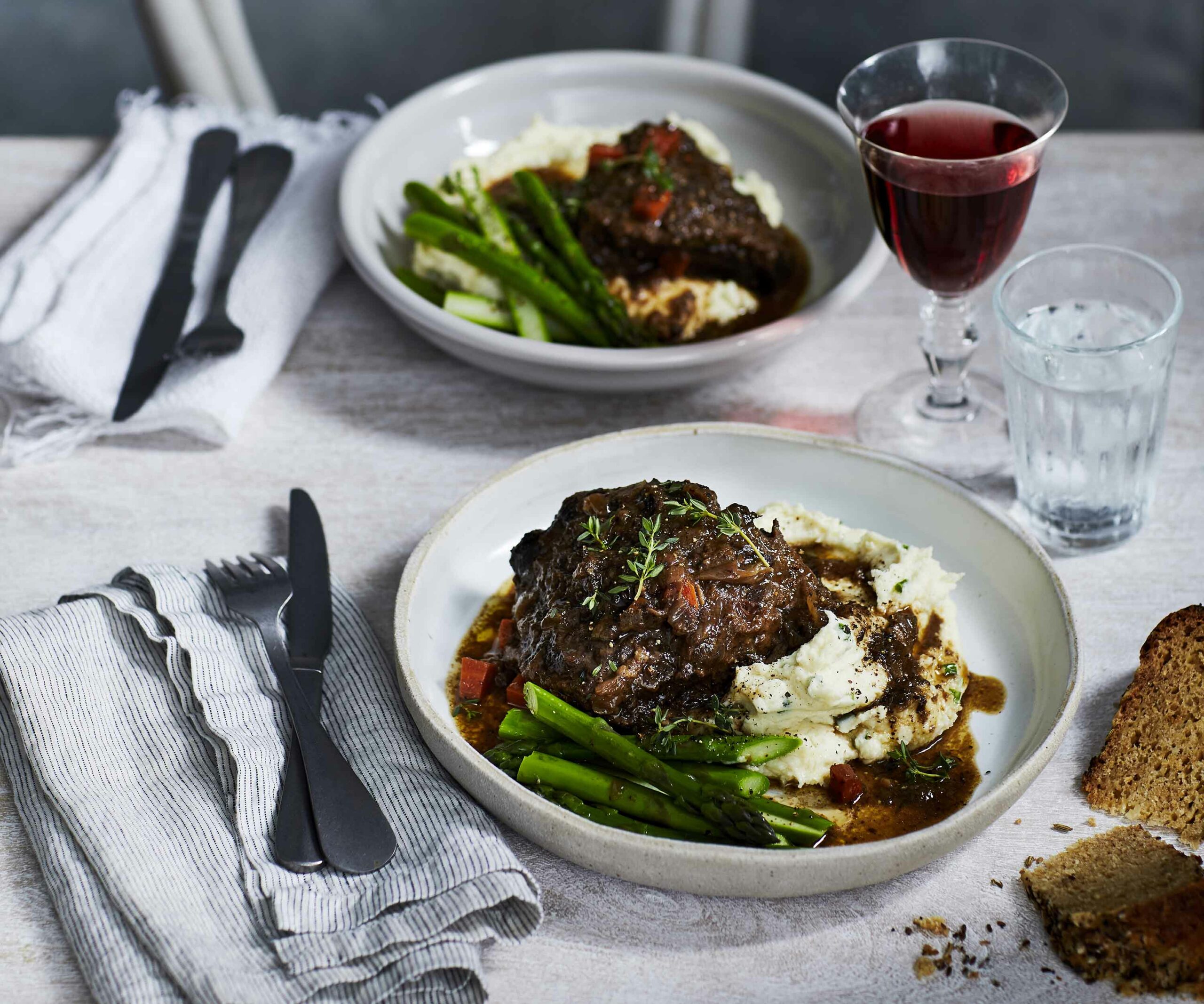 two bowls filled with beef cheeks, beans and mash on a set table