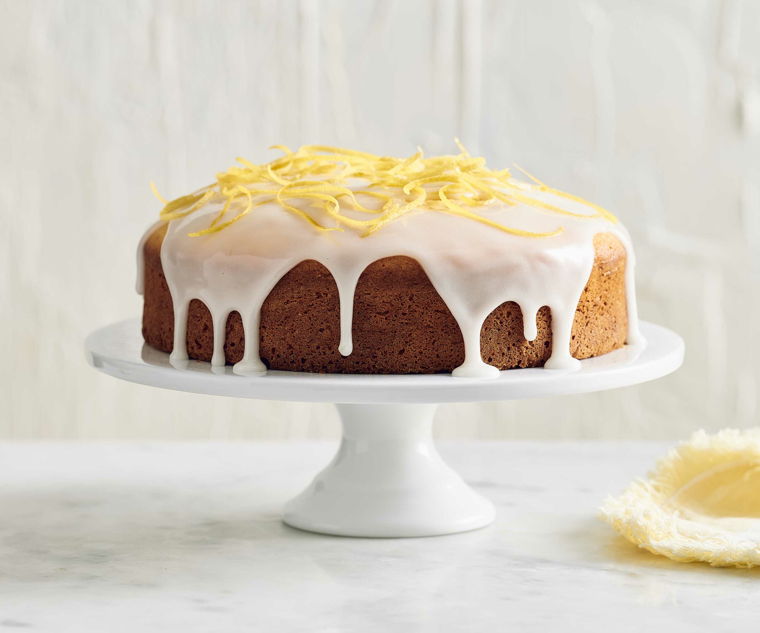 lemon cake topped with lemon icing on a cake stand