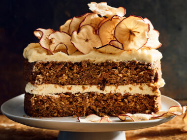 A slice of apple and carrot cake with brown butter icing and dried apple slices on top